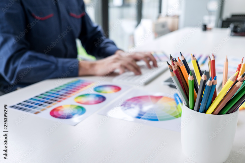 Poster Image of male creative graphic designer working on color selection and drawing on graphics tablet at workplace with work tools and accessories