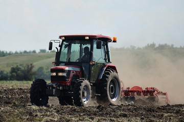 Obraz premium Brand new red tractor on the field working. Tractor cultivating soil and preparing a field for planting