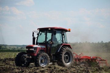 Fototapeta premium Brand new red tractor on the field working. Tractor cultivating soil and preparing a field for planting
