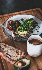 Healthy vegan summer lunch. Avocado toast on sourdough bread with chives, coriander and cherry-tomatoes with cup of coffee on wooden board. Vegetarian, dieting, alkiline diet, clean eating concept