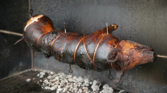 pig spinning on spit - cooking pork in firewood grill. roast suckling pig is cooked