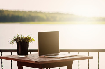 A relaxed and sentimental scene on a balcony with a laptop and a plant on a wooden terrace table, near ocean in archipelago in Porvoo Finland