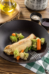delicious portion of golden deep fried sea fish served on brown plate with mix of cooked carrots and romanesco