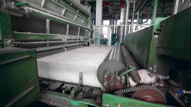 Factory machines roll polyester fiber on a conveyor.