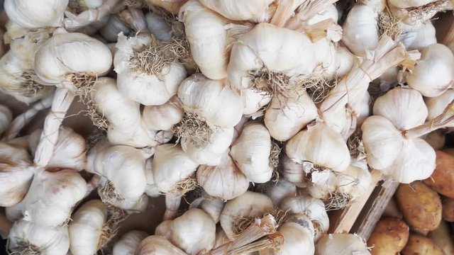 Top view slow motion tracking shot over a pile of many white garlic bulbs on display at a farmers street market.