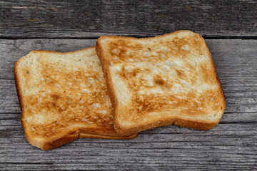 Two square ruddy pieces of bread for toasts on the old gray wooden background