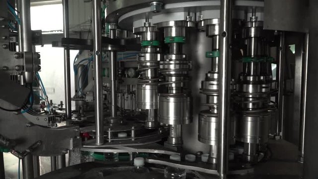 Production line of plastic bottles. Machine for filling water and twisting plastic bottles with lids. The machine twisting caps. Plastic bottles travel up through the plant.
