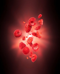 Whole and sliced fresh raspberries in the air with flash of light in the dark