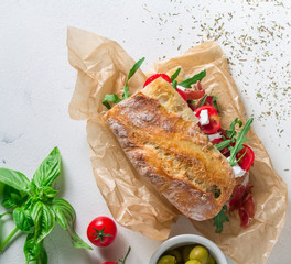 Sandwich from baguette, ham and prosciutto, soft cheese, arugula and tomato parchment on a light background. Top view