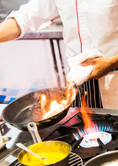 Chef cooking with flame in a frying pan on a kitchen stove.