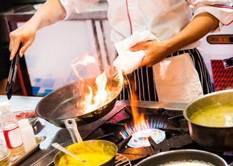 Chef cooking with flame in a frying pan on a kitchen stove.