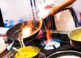 Chef cooking with flame in a frying pan on a kitchen stove.