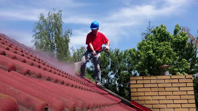 House roof cleaning with water pressure tool. Worker on top of building washing tile with professional equipment. Moss removing.