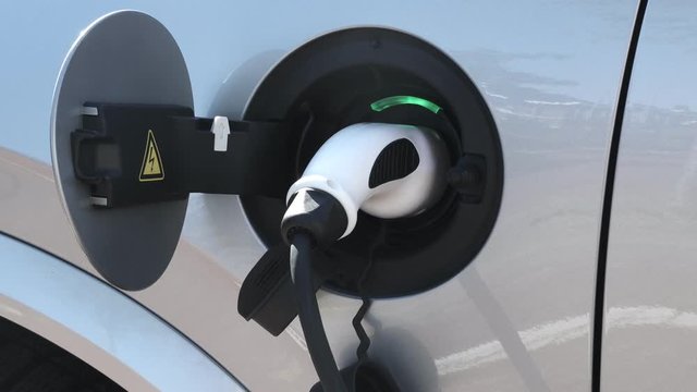 EV car or electric car at charging station with the power cable supply plugged in. Green light indicator of charging batery. Friendly electro mobility environment.