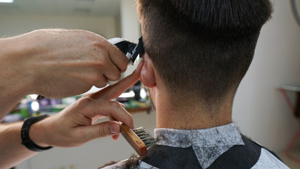 Barber cutting young man hair with clipper.Men's grooming trimmer in a beauty salon. Hair dressing concept.