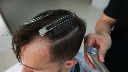 Closeup of hairdresser cutting man's hair in barber shop.Male hairstylist serving client, making haircut using hairpins and hair clips and comb.