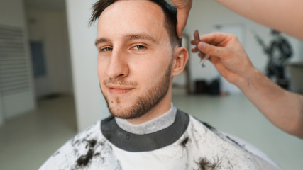 Making hair look magical. Portret of young Bearded man sitting in chair at barbershop. Barber is trimming his hair with a straight razor. Closeup. 