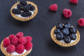 Basket-shaped cookies with raspberry, blueberry and blackberry berries. Black background