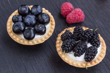 Basket-shaped cookies with raspberry, blueberry and blackberry berries. Black background