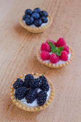 Basket-shaped cookies with raspberry, blueberry and blackberry berries. Wooden background
