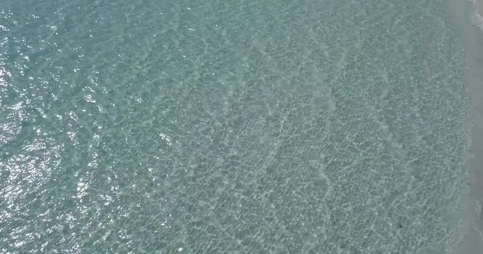 AERIAL 4K Camera movement backwards above water surface with light reflections and small ripples
