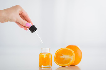cropped view of woman holding dropped near bottle with orange essential oil and fresh oranges on white background
