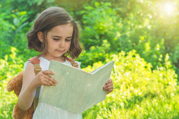 Cute industrious child is standing with a book and a briefcase outdoors. Little Girl reading the...