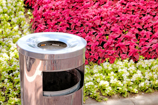 trash can with cigarette in ashtray at outdoor street smoking area against red white green flowers background closeup view of metal bin for garbage collecting