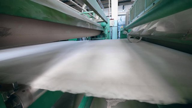 Plant conveyor moves polyester batting, pressing it.
