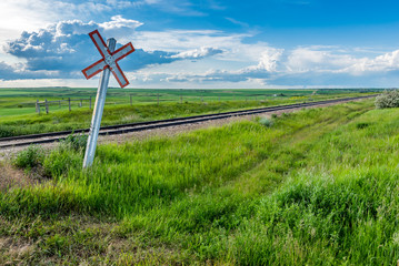 Prairie railway crossing sign and tracks with storm clouds on the horizon in Saskatchewan, Canada