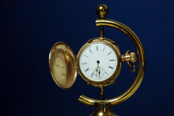 Antique Gold Pocket Watch on a display stand against a dark blue background.