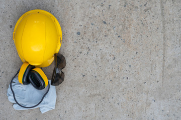 Safety Work and Protective Equipment concept. Safe Health Industry Tools. Yellow hard hat, safety ear muffs, protective gloves and goggles on concrete background.