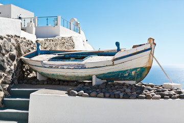 Fototapeta na wymiar Old boat on a terrace with view on the white architecture of Santorini, Greece
