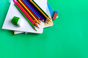 School set of notebooks, pencils, an eraser and sharpeners on a green background with copy space.