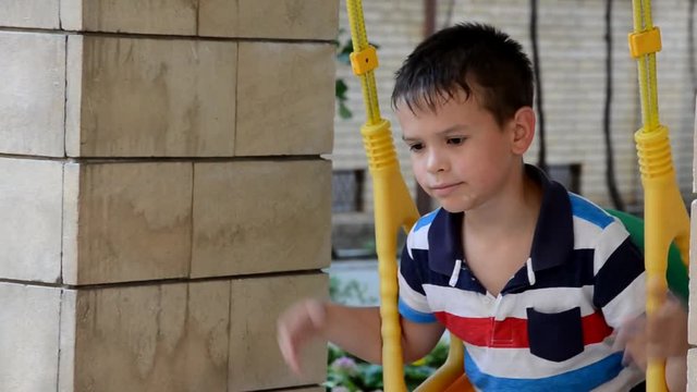 A young boy swing set in a park. The small child is having fun, smiling. It is summer time at the playground. He is wearing a t-shirt and shorts and is laughing.