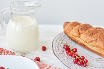 Different ingredients for breakfast. Croissants on plate on the wood board, berries, coffee, milk and honey on a white tablecloth. Traditional French breakfast. Top view
