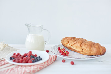 Different ingredients for breakfast. Croissants on plate on the wood board, berries, coffee, milk and honey on a white tablecloth. Traditional French breakfast. Top view