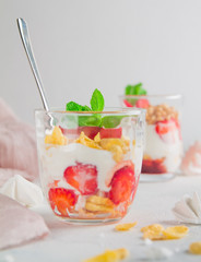 milky dessert in glass cups with strawberries airy colorful bize decorated with leaves of fresh mint on a white background
