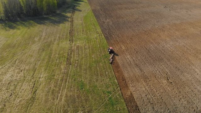 Aerial view of a powerful, energy-saturated tractor of red color with a large hook force pulling a multi-turn plow, cultivator with ploughshares on the background of picturesque nature. Tillage before