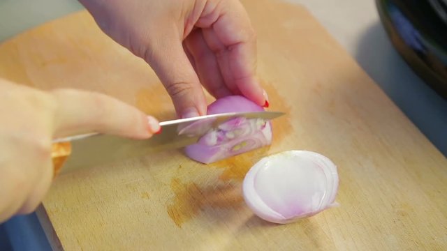 Woman knife red onions on a wooden board
