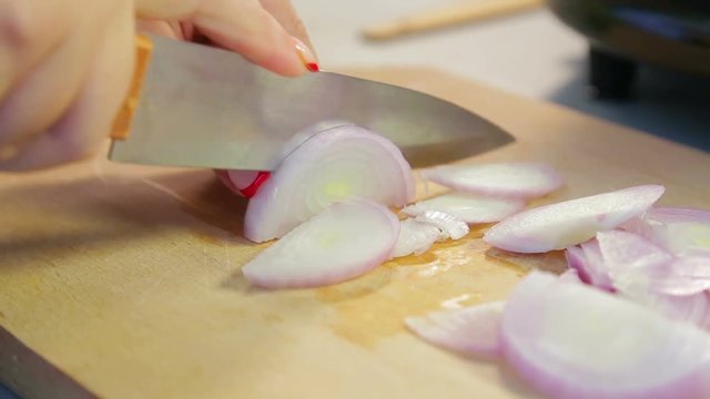 Woman knife red onions on a wooden board.