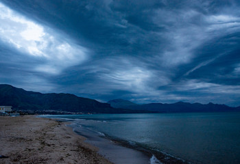 Fototapeta na wymiar Scenic gray-blue clouds during sunrise over coastline with sandy beach and clear sea water in Alcamo Marina, small town in Sicily, Italy, summer vacation destination