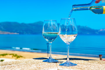 Waiter pouring white wine in wine glasses on outdoor terrace witn blue sea and mountains view on background