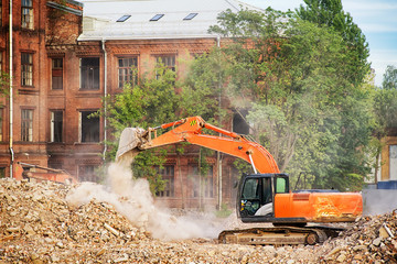 Orange excavator working on the ruins of a demolished building
