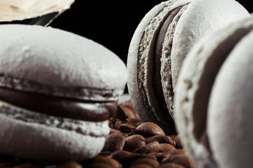 French macaroons isolated with coffee beans. Selective focus. macaroon in gray tone. Beautiful macaroons on black background. Stylish arrangement sweet. Flat lay, top view. Macro photo.