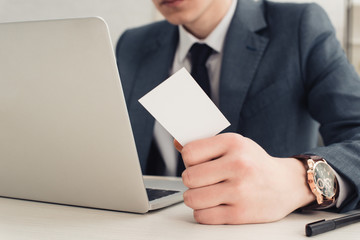 partial view of businessman holding empty business card while using laptop