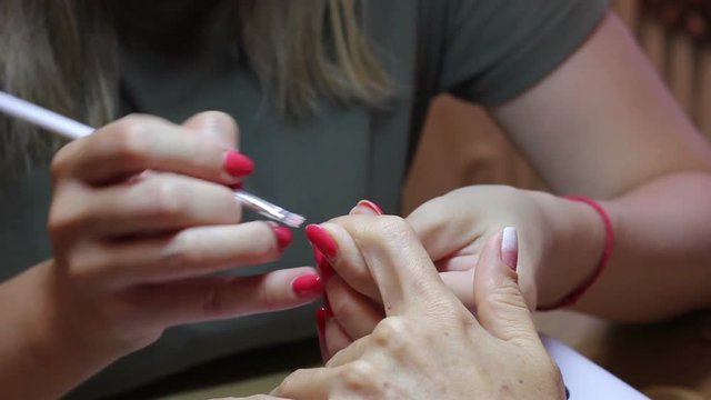 Female nail painting. Manicure master creating a gradient with a brush on client forefinger nail. Close up view. Thin beautiful fingers of female hands and body of manicure master in frame.