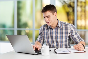 Happy young man works on his laptop with coffee at the table