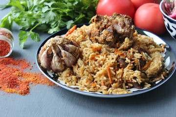 The concept of Oriental cuisine. Homemade Uzbek lamb pilaf is served on a round platter. Fresh herbs, vegetables, and spices for cooking pilaf. Copy space.