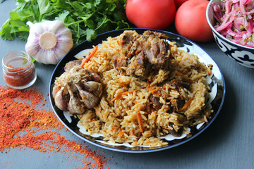 The concept of Oriental cuisine. Homemade Uzbek lamb pilaf is served on a round platter. Fresh herbs, vegetables, and spices for cooking pilaf. Copy space.